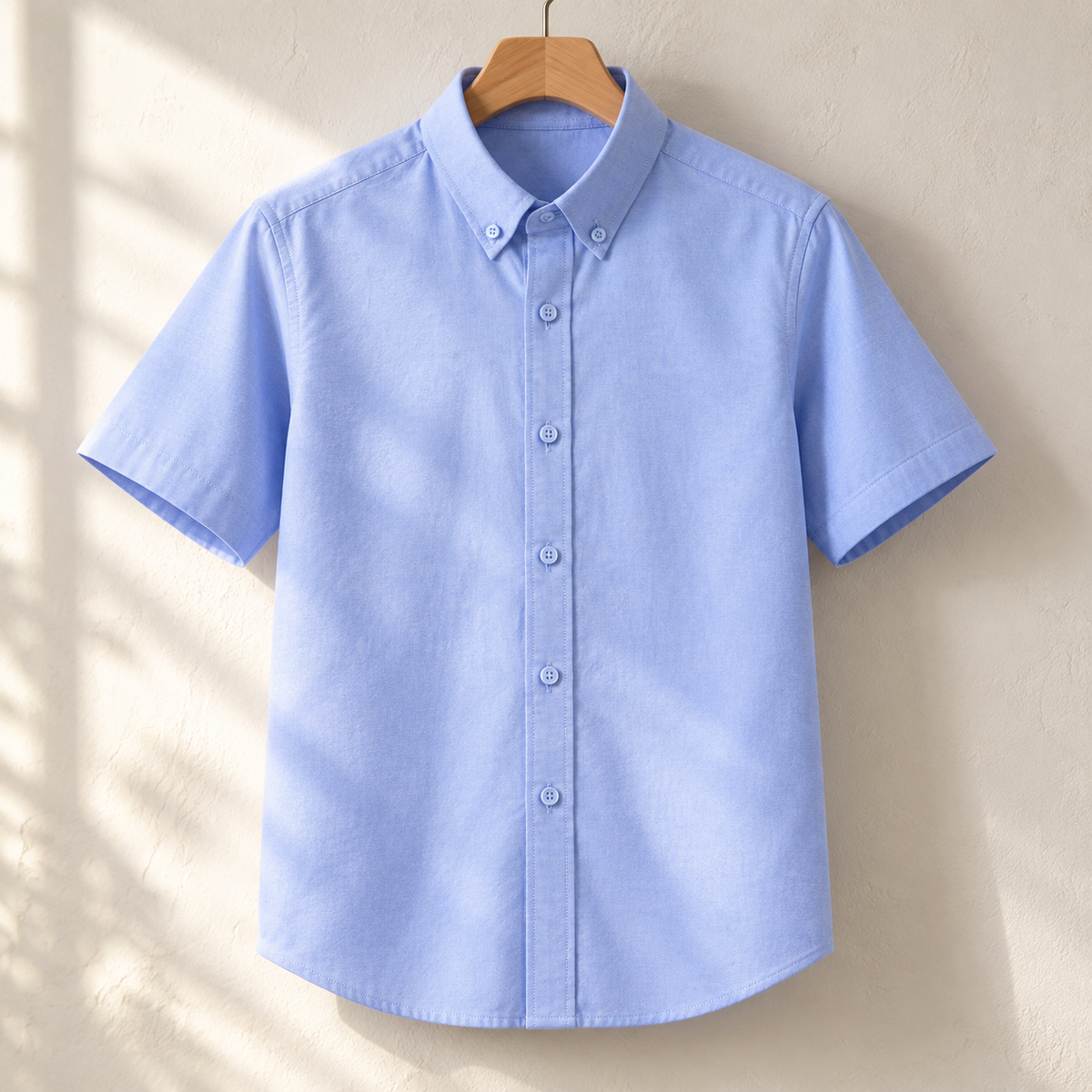 Light blue oxford shirt on a wooden hanger against a plaster wall