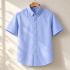 Light blue oxford shirt on a wooden hanger against a plaster wall